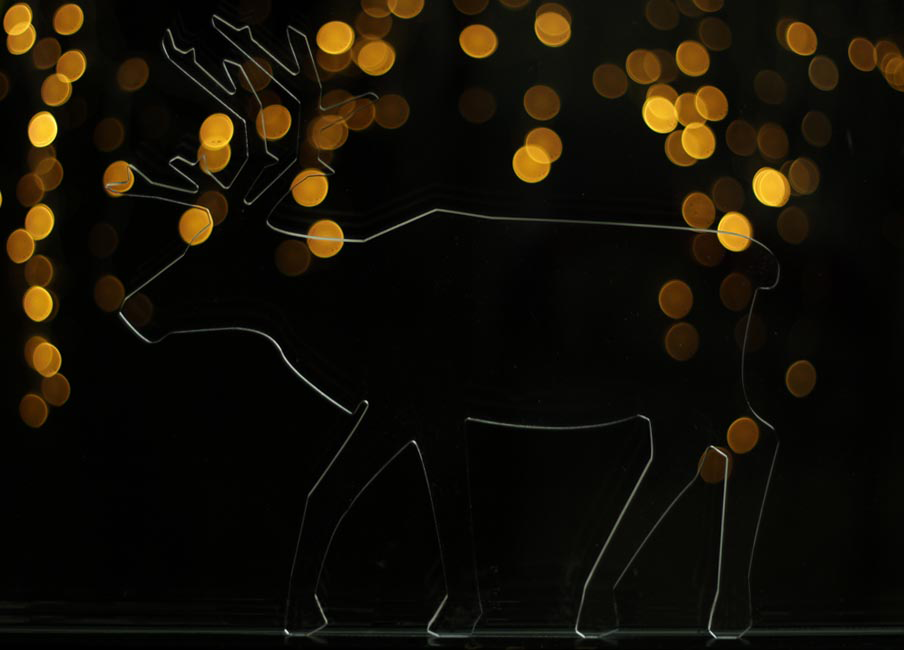 A silhouetted reindeer in acrylic glass against a backdrop of fairy lights 